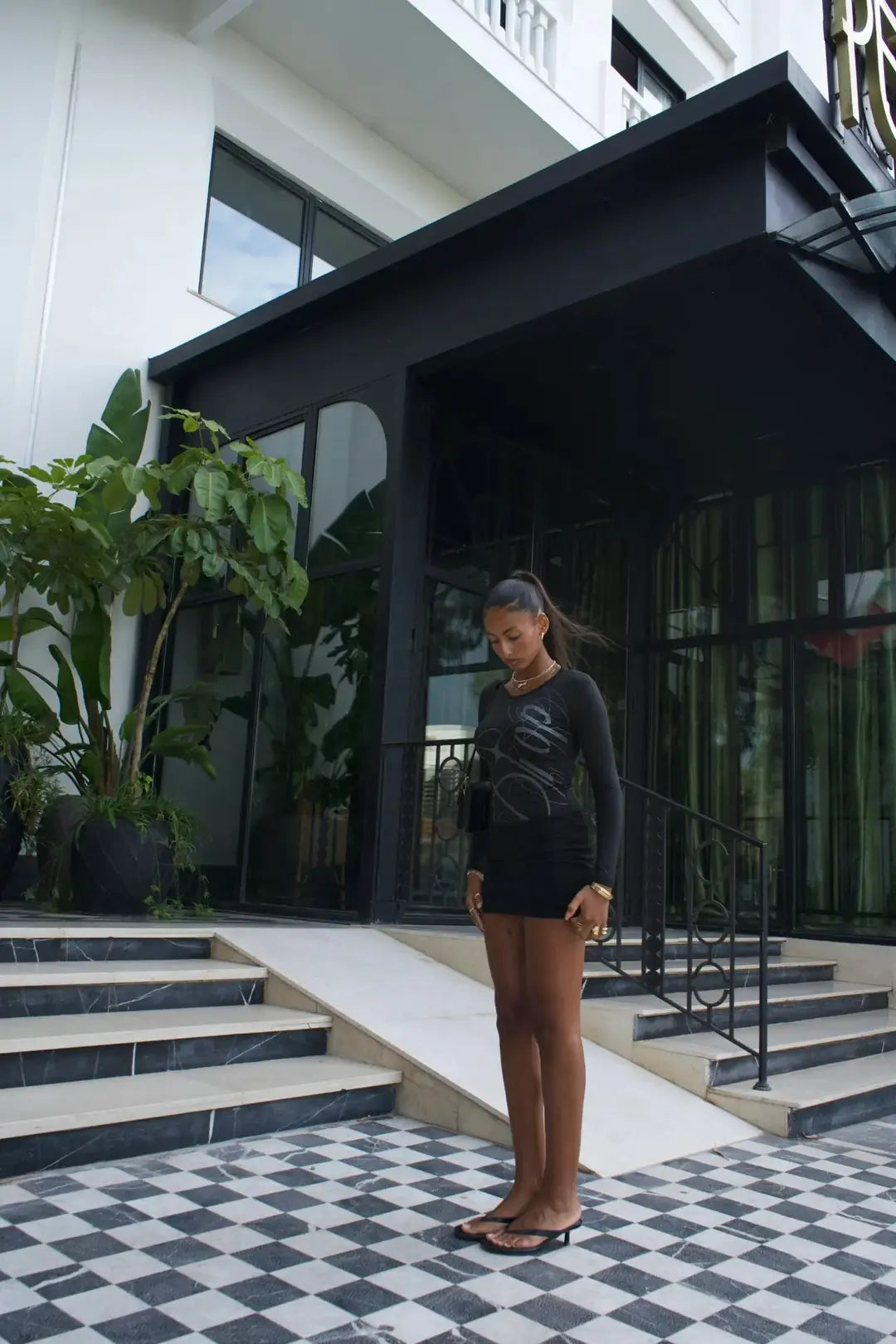 Model wearing the black DROP bodysuit in a tiled courtyard