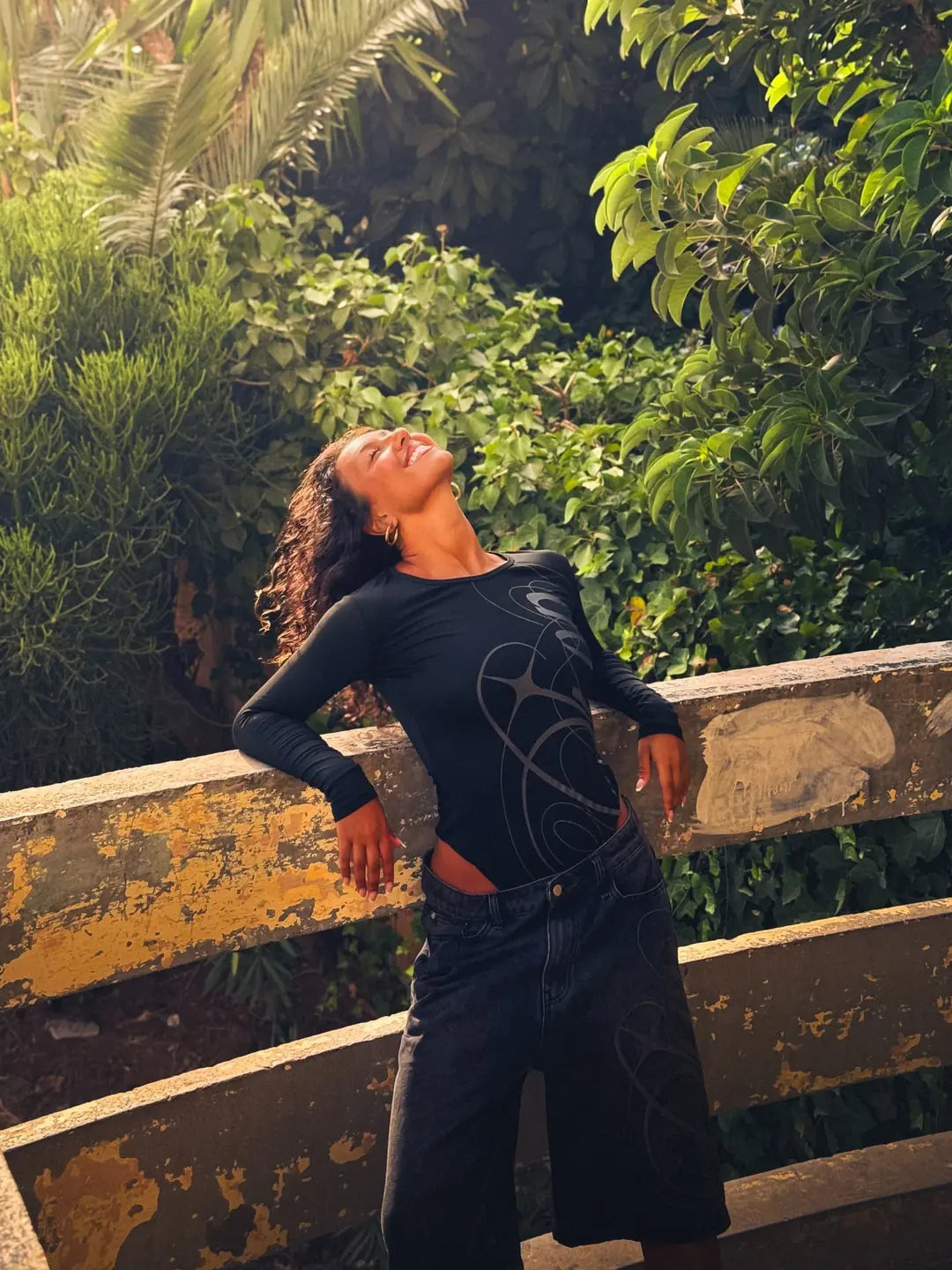 Model in the black DROP bodysuit and denim jorts in the garden